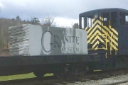 A flat train car with a large block of granite stone on it with the words vermont granite museum carved on it